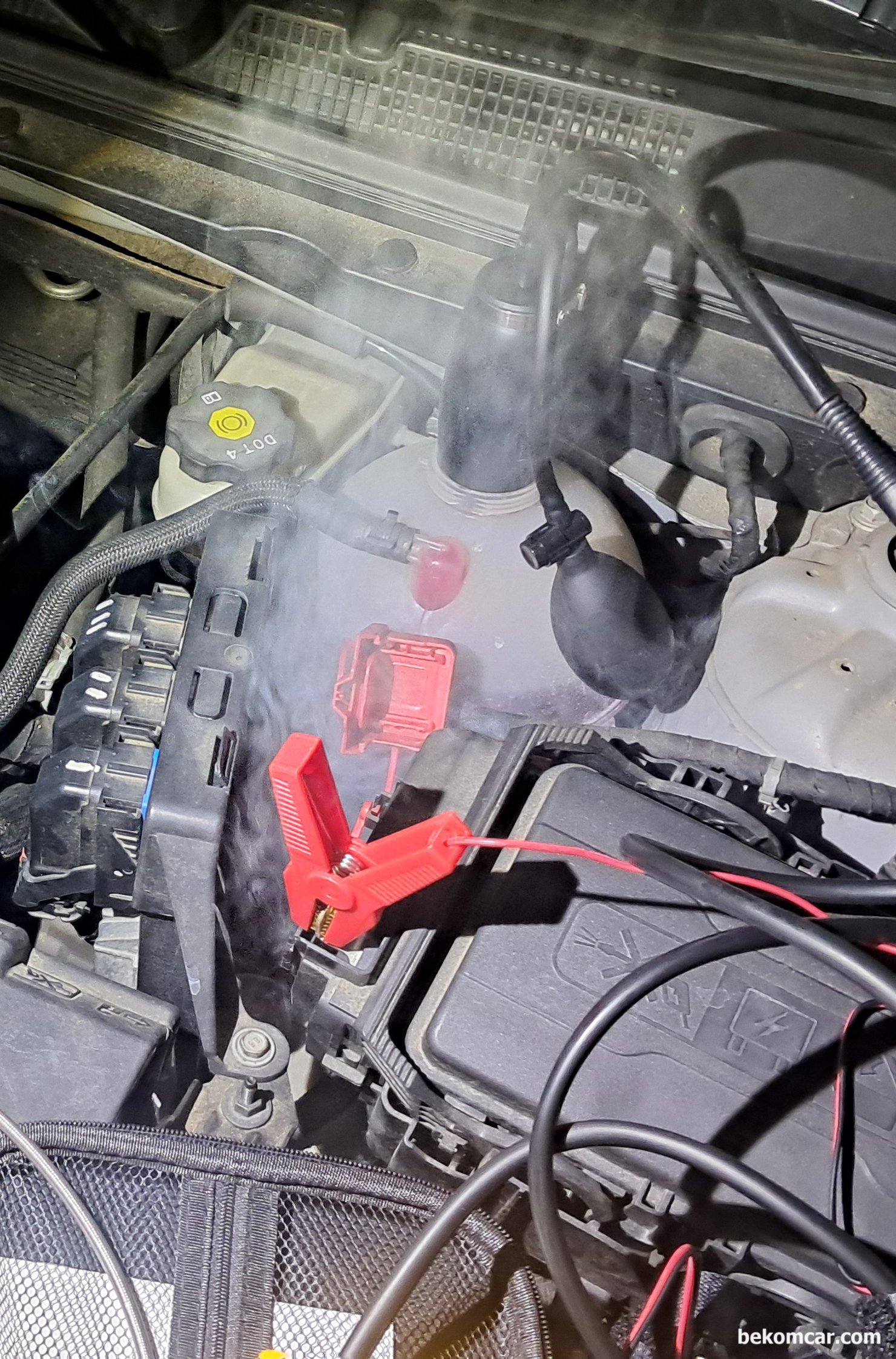 쉐보레 말리부 1.5T 실린더내시경 및 헤드가스켓 냉각수리크 진단과정 기록, 헤드 개스킷 누스 점검을 위하여 스모크 머신 세팅을 하고 있다. 냉각수 보조 통에 연기와 압력을 주고, 엔진 헤드와 블록 사이에서 냉각수가 흘러나오는지 확인하는 과정이다. 그런데 예상 못 한 변수가 발생, 냉각수 보조 통 아래쪽에서 상당한 연기가 나오고 있다. 자세히 보니 물방울이 보이고 냉각수가 아주 조금씩 새어 나오고 있다. 헤드 개스킷 누수 측정 차량은 쉐보레 말리부 1.5T 에코텍 엔진이다.|贝科姆汽车 (bekomcar)